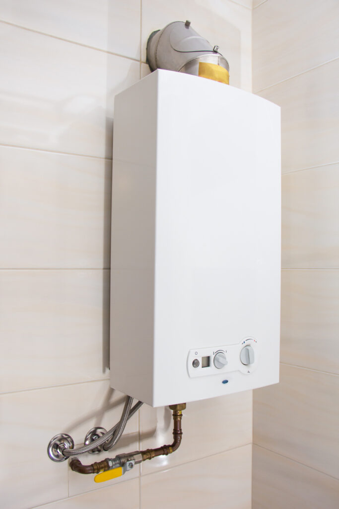White tankless water heater installed on a white tile wall.
